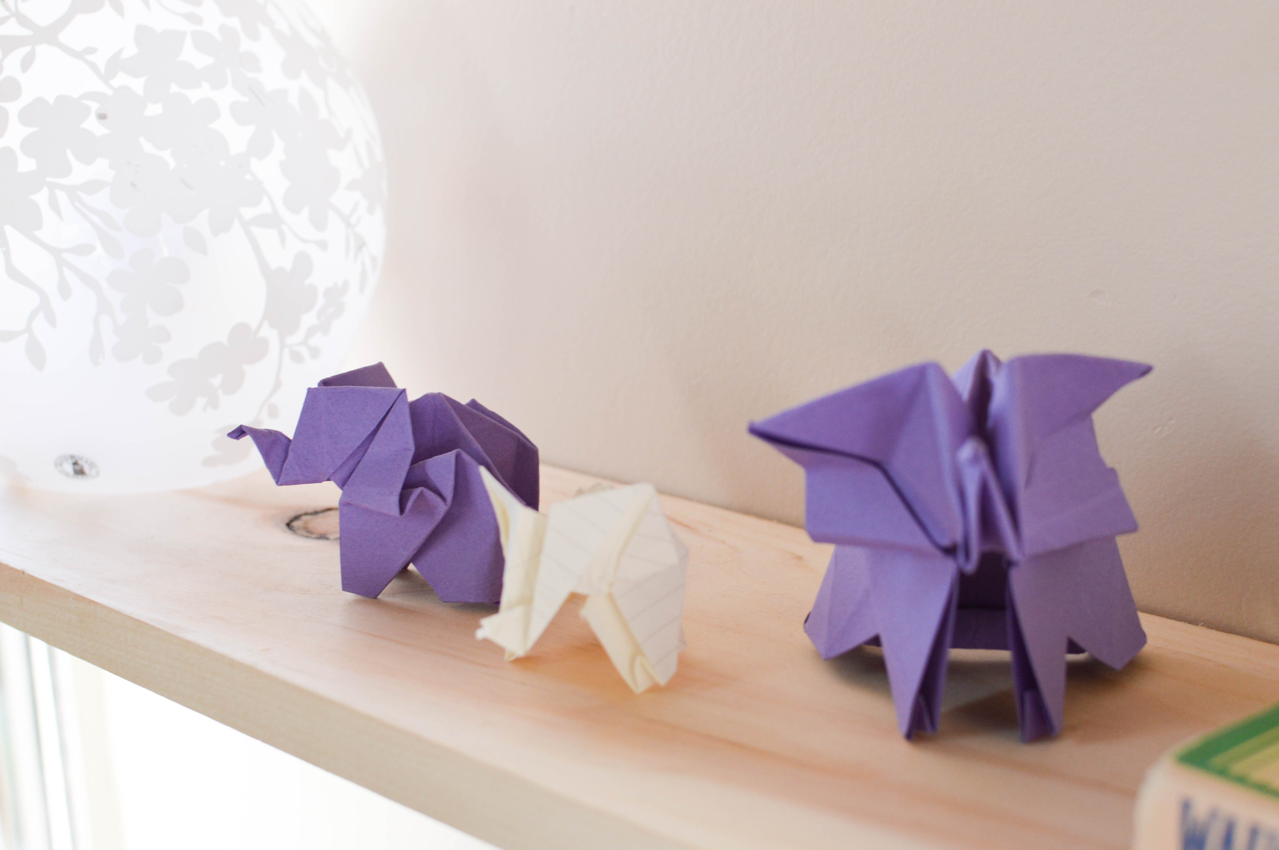 Origami elephants sit on a wooden shelf